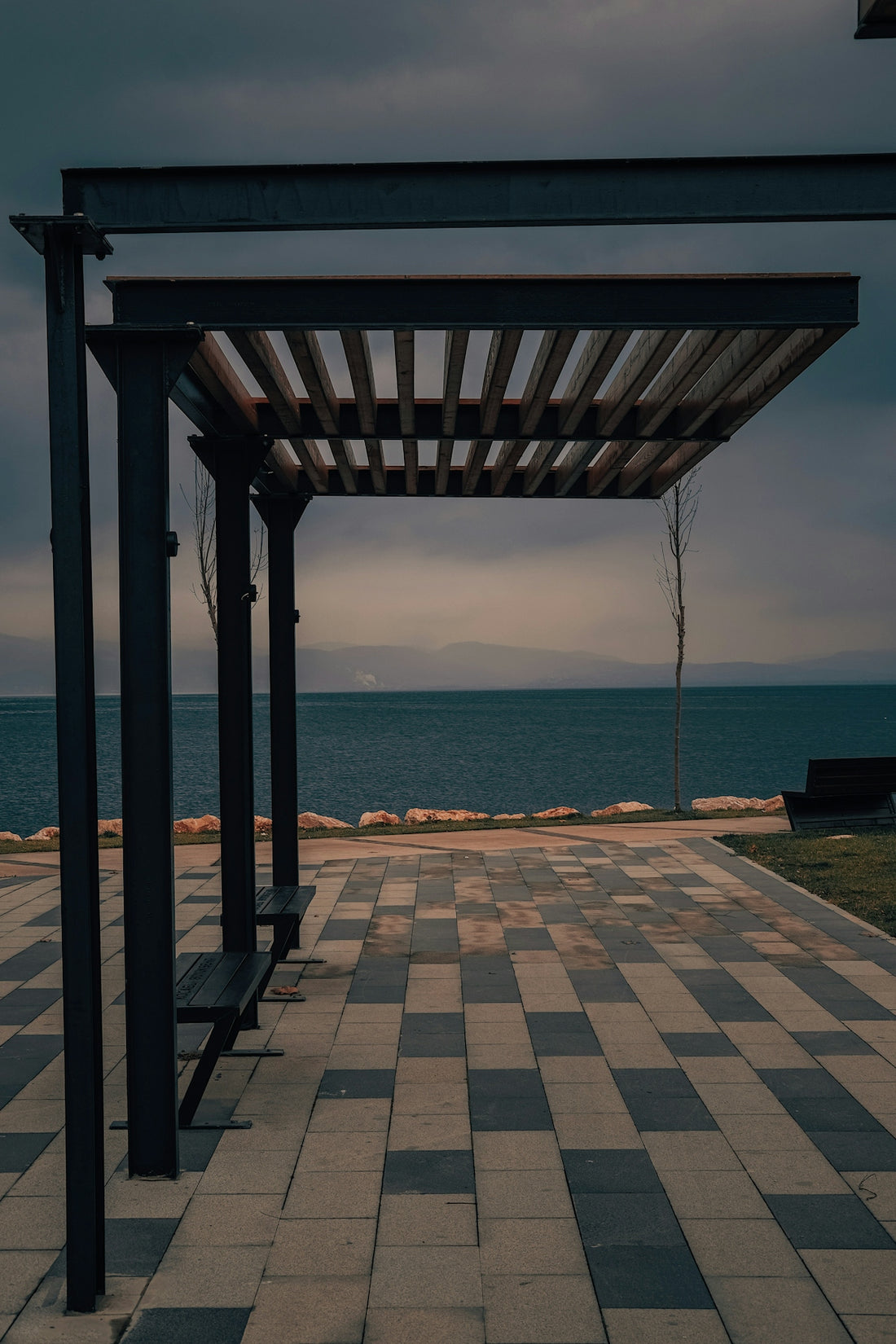 a bench sitting on top of a tiled walkway next to the ocean