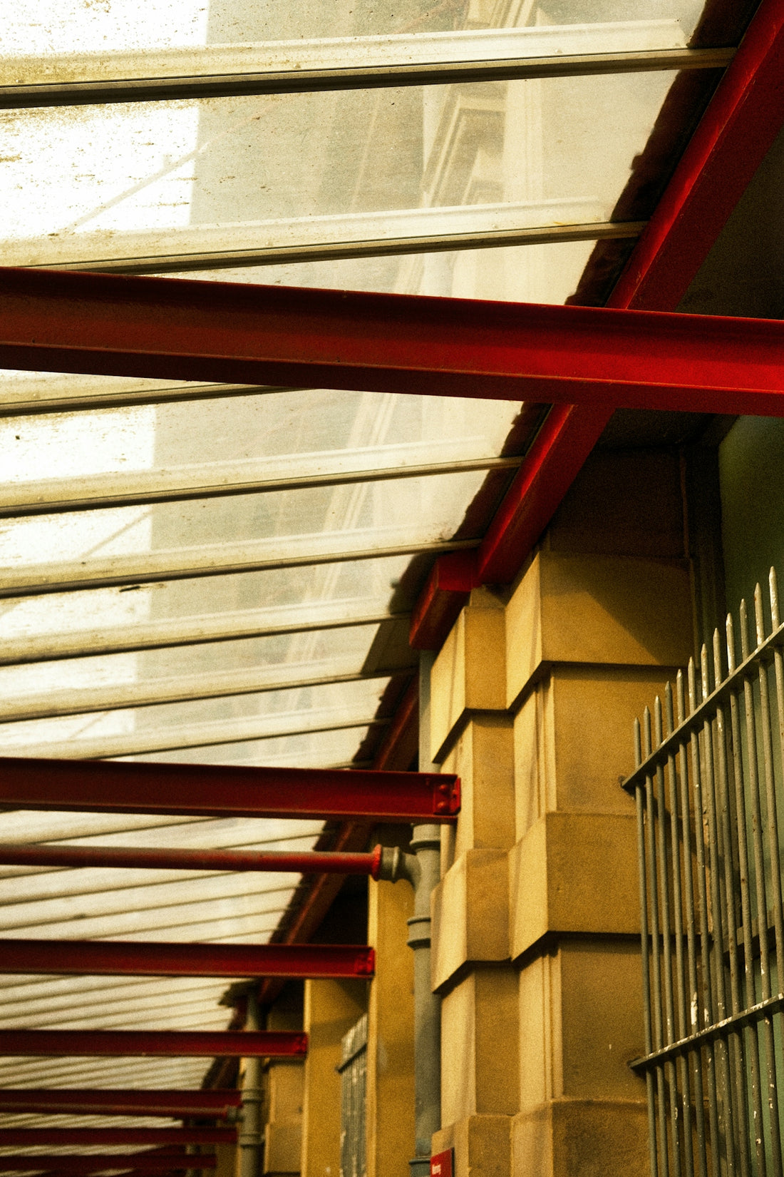 Red beams support a glass roof over stone building.